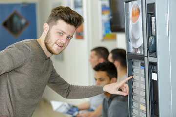 young man choosing drink from vending machine - obrazy, fototapety, plakaty