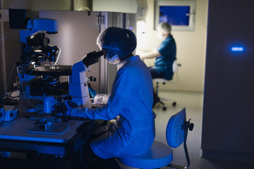 In a Modern Laboratory Scientist Conduct Experiments. Chief Research Scientist Adjusts Specimen in a Petri Dish and Looks on it Into Microscope.