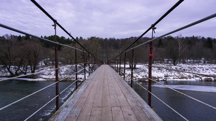 Obraz premium Winter landscape with river and suspended pedestrian bridge