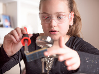 Little girl with safety glasses works with a soldering iron on a computer component