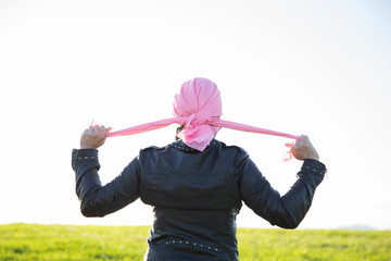 Woman tying a pink handkerchief on her head.