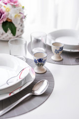Minimalist white tableware on a white surface dining table in daylight, angled view