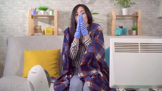 Freezing young asian woman sitting with heaters in the living room