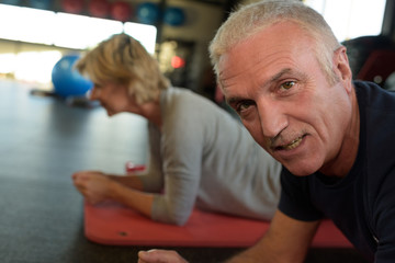senior couple in gym in plank position working abs