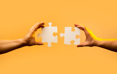 Closeup hand of connecting jigsaw puzzle. Business solutions, success and strategy concept. Two hands trying to connect couple puzzle piece on yellow background. Holding puzzle. Teamwork concept - obrazy, fototapety, plakaty