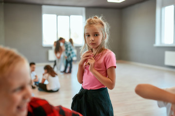 Dance school. Portrait of a little cute girl looking at camera while standing in the dance studio. Group of children having a choreography class