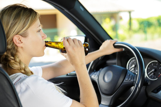 Woman Drinking From A Beer Bottle While Driving Car