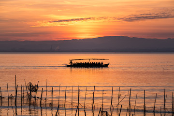 Sunset pier Albufera Valencia tourist ride boat reflections orange sky in the lake Naural Park Spain. traditional fishing nets in the water