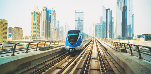 Metro train on Red line in Dubai downtown with skyscrapers at background.