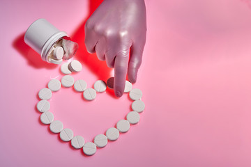 Heart sign made from white pills on pink background. Doctor takes a white pill for the heart.