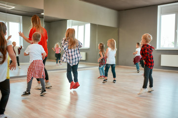 Choreography class. Group of active children dancing in front of the large mirror while having choreography class in the dance studio. Female dance teacher and kids
