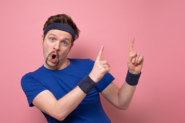 Excited sportive young man in blue t-shirt and hair band cheering and pointing on copyspace