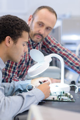 technician using magnifying glass for analyzing computer mainboard