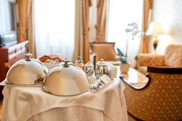 Service that you deserve. Luxurious Room Service. Breakfast in luxury hotel room delivered by waiter. Meals under silver cloche. Hospitality and vacation concept