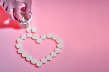 Heart sign made from white pills on pink background, flat lay with space for text. Doctor takes medicine from a bottle.