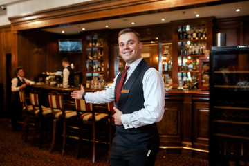 For your enjoyment. Portrait of smiling waiter welcoming guests in hotel restaurant - obrazy, fototapety, plakaty