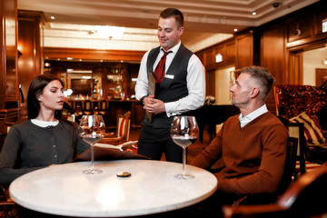 Service is our main purpose. Confident waiter giving menu to costumers. Couple having dinner in hotel restaurant