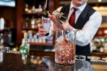 Know how to do it. Cropped shot of young bartender standing at counter and pouring red wine to prepare iced cocktail in the bar