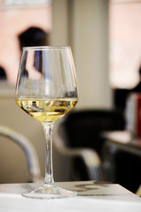 Close-up of a glass of white wine on a bar's table outside. Background out of focus