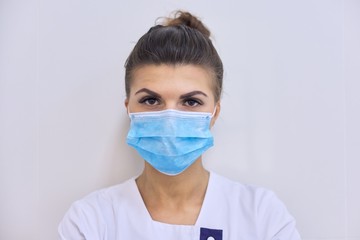 Young serious woman doctor in medical mask looking at camera