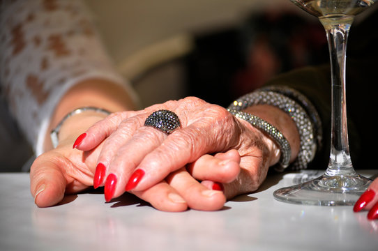 Elderly mother holding daughter's hand on a restaurant table with a glass of white wine next to them. Day time sharing with the mother. Hands holding each other. - Powered by Adobe