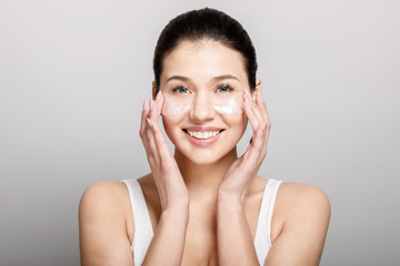 Smiling young cute girl using pore strips on her cheekbones isolated light background