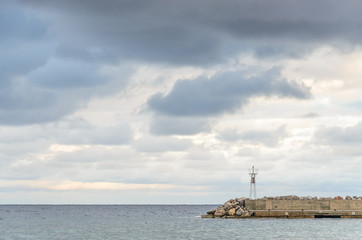 A concrete breakwater with a beacon on a calm overcast day