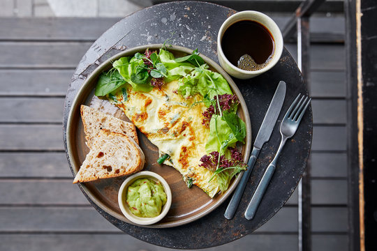 fried eggs with basil, salad and herbs, sauce and white bread, a cup of coffee, amlet, knife and fork, on a table