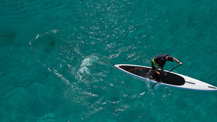 Aerial drone photo of fit man practising Stand Up Paddle or SUP in tropical exotic bay with emerald sea
