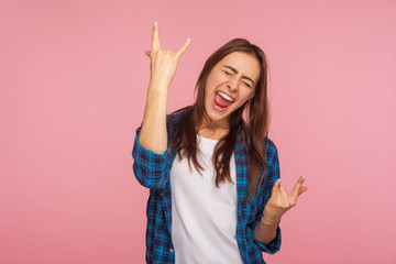 Portrait of enthusiastic overjoyed girl in checkered shirt showing rock and roll gesture and...