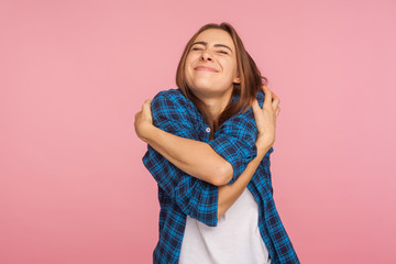 I love myself! Portrait of charming girl in checkered shirt hugging herself tightly and smiling with pleasure, appreciating her appearance, self-esteem concept. studio shot isolated on pink background