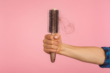 Closeup of female hand holding brush with unhealthy damaged brunette hair against pink background, hair loss problem, dandruff and alopecia illness. indoor studio shot isolated, copy space for ad text