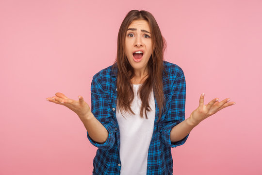 How could you? Portrait of indignant girl in checkered shirt raising hands asking what why, looking with dissatisfied disappointed expression, making claims. studio shot isolated on pink background