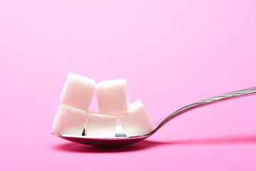 Sugar cubes on a spoon on a pink background