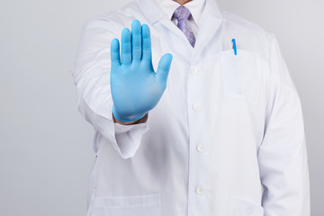 male doctor in a white coat and blue sterile gloves shows a stop gesture