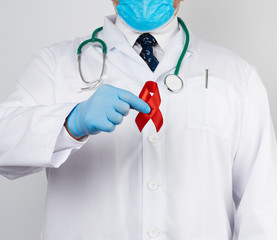 doctor in white uniform and sterile latex gloves holds a red ribbon-symbol of the fight against disease AIDS