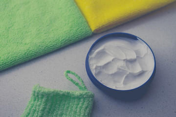 Opened round container with white cream on a table with towels.