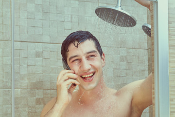 Smiling white man uses phone in a shower stall.