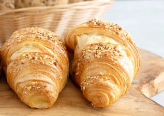 Fresh traditional french croissants closeup sprinkled with nuts, lie on a wooden board. In the background is a wicker basket with buns. Fresh bakery. Making bread
