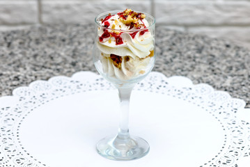 Dessert in a glass of whipped cream with nuts and strawberry syrup on a white napkin
