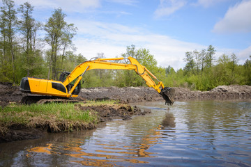Excavator near small river or pond in countryside. Cleaning river from garbage