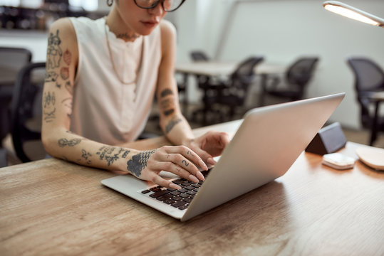 Busy lady. Cropped photo of young tattooed businesswoman using laptop while working in the modern office