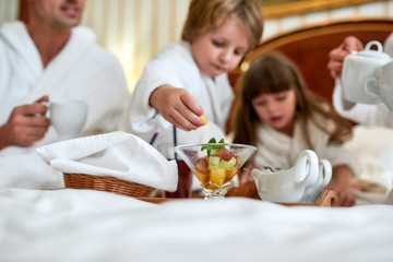 Obraz na płótnie Canvas Eat good. Family in white bathrobes having breakfast in bed. Focus on fruit cup on the tray. Healthy food, resort, room service concept
