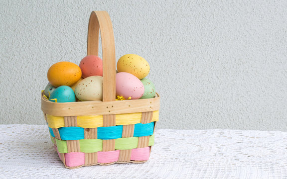 a colorful wicker Easter basket filled with speckled Easter eggs on a lace tablecloth with copy space