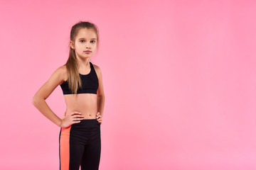 Health and Fun. A cute kid, girl is engaged in sport, she is looking at camera while getting ready to exercise. Isolated on pink background. Fitness, training, active lifestyle concept.