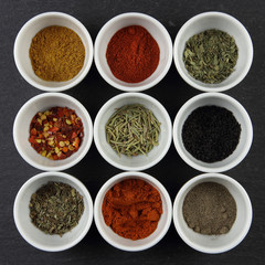 Overhead photo of nine white bowls with different spices