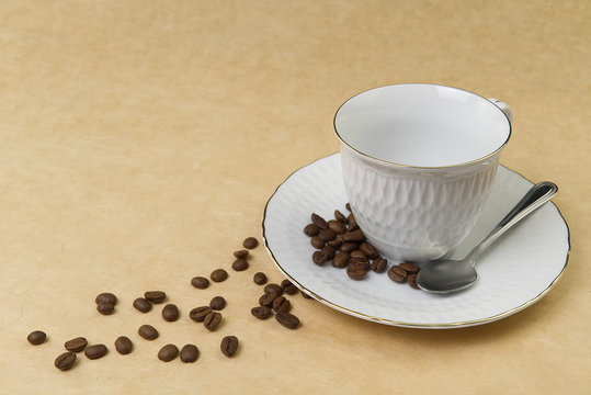 Empty white coffee cup with gold border and coffee seeds on the table. close up