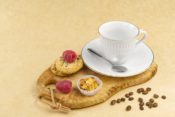 Empty white coffee cup with a gold border on olive wood board. Breakfast setting, coffee oatmeal cookies with raspberries and mini tosca cake