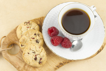 White coffee cup with a gold border on olive wood board. Breakfast setting, coffee oatmeal cookies with raspberries