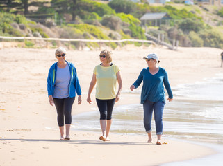 Three happy senior women walking and exercising together on beach. Retirement and healthy lifestyle